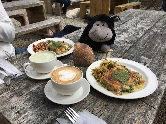 Two lunch plates, a latte and a matcha on an outdoor table, with a black toy sheep sitting beside them