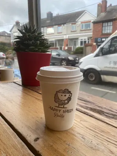 A Happy Sheep takeaway cup on a wooden window ledge, looking out on the street